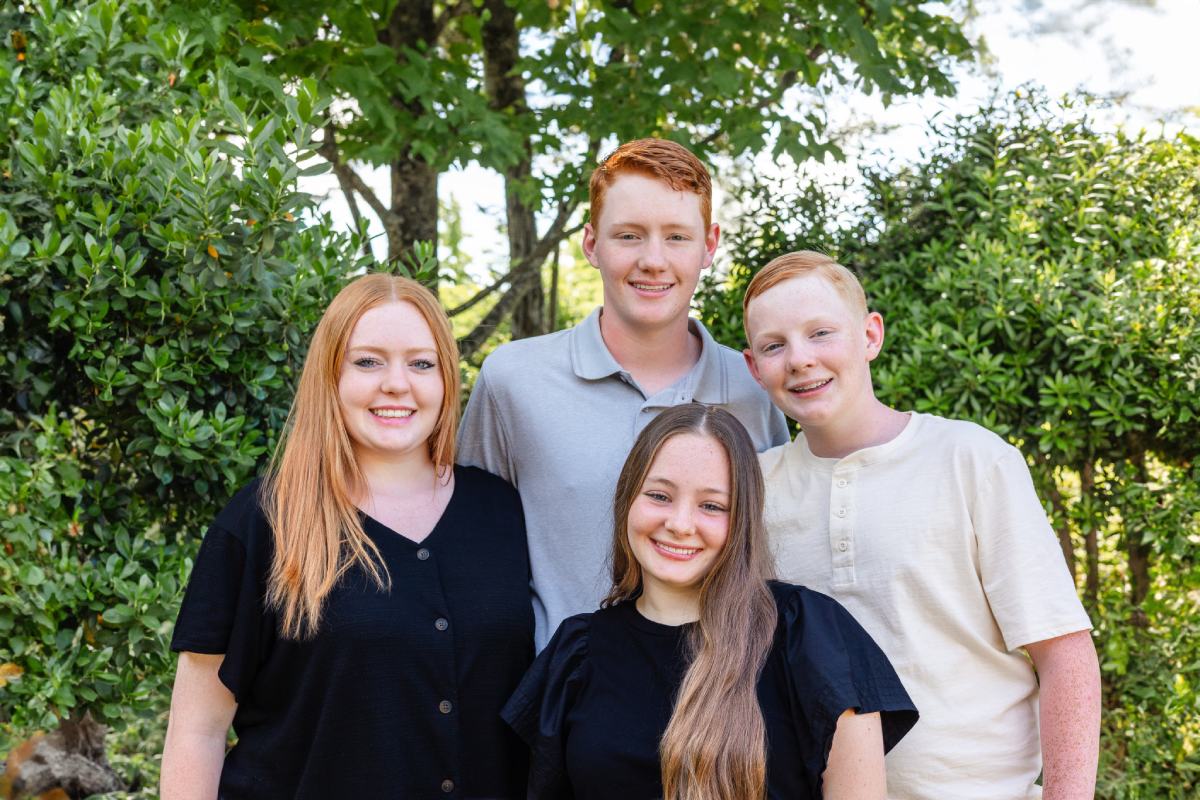 A group of four young people smiling and posed with bushes behind them