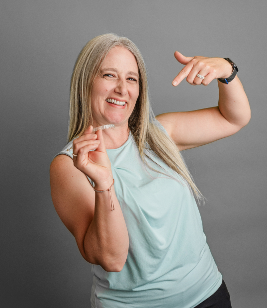 A woman holding up an aligner and smiling