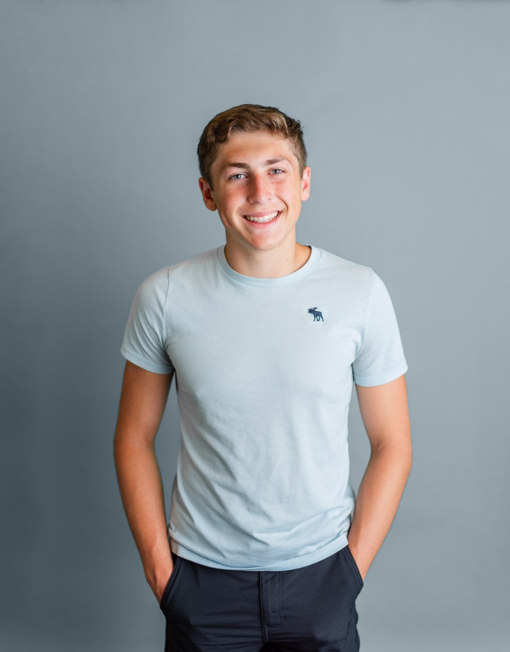 A young man standing with his hands in his pockets and smiling